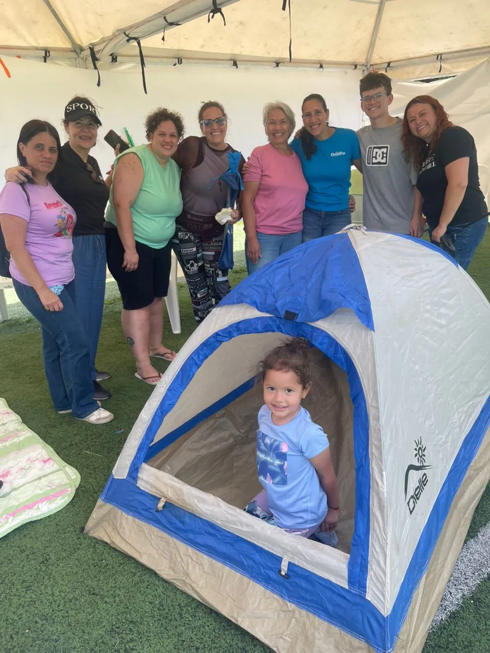 Una niña sonríe dentro de una carpa recién entregada, rodeada de su familia y del equipo de entrega
